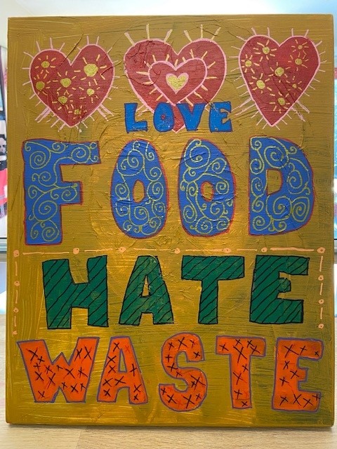 Photo of a colourful painted sign that reads "Love Food Hate Waste" with love hearts across the top