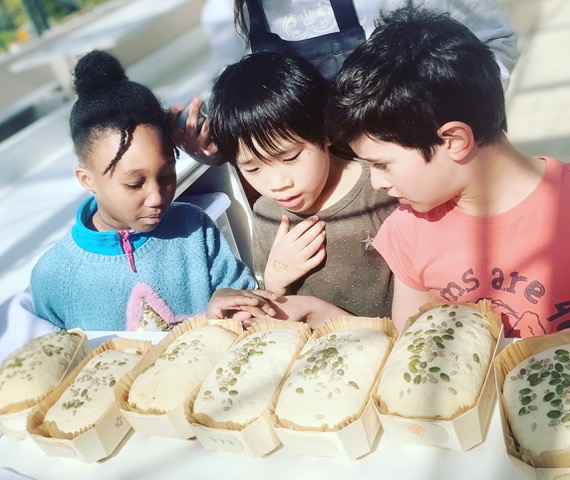 Photo of three children looking at freshly baked loaves of bread on the table in front of them
